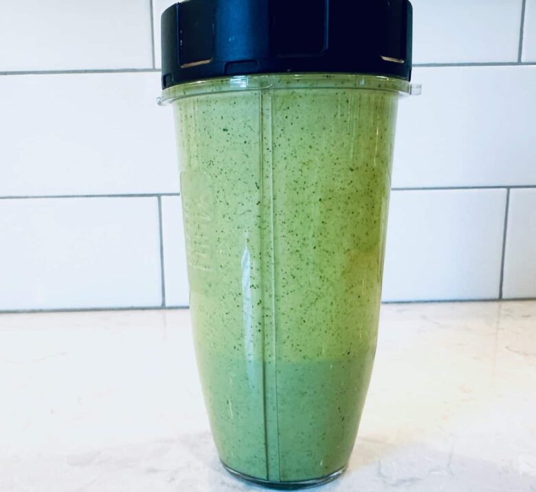 A clear blender cup filled with green dressing to make southwest chopped salad on a light countertop.