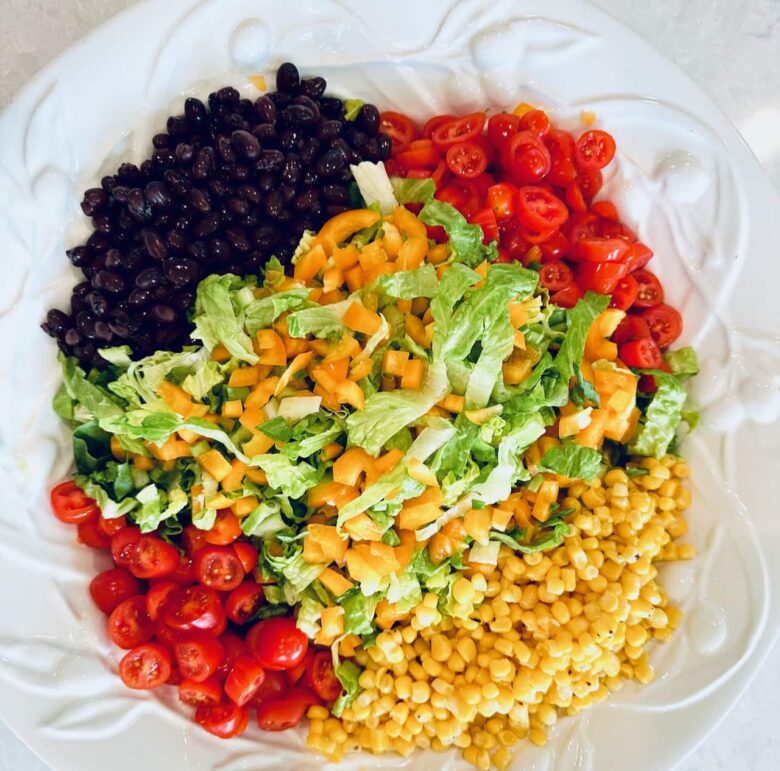A bowl with salad ingredients to make southwest chopped salad, including lettuce, black beans, grape tomatoes, and corn.