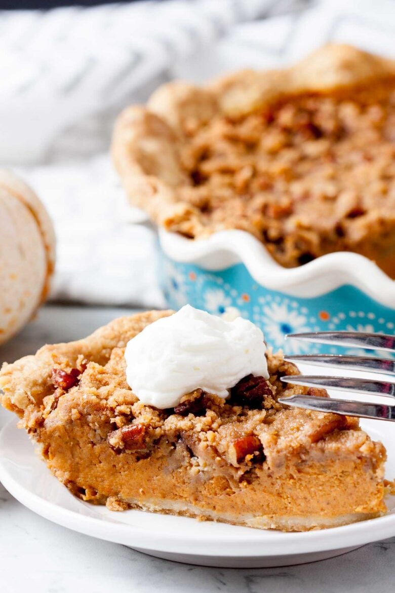 A closeup shot of a slice of pumpkin pie with streusel topping on a plate.