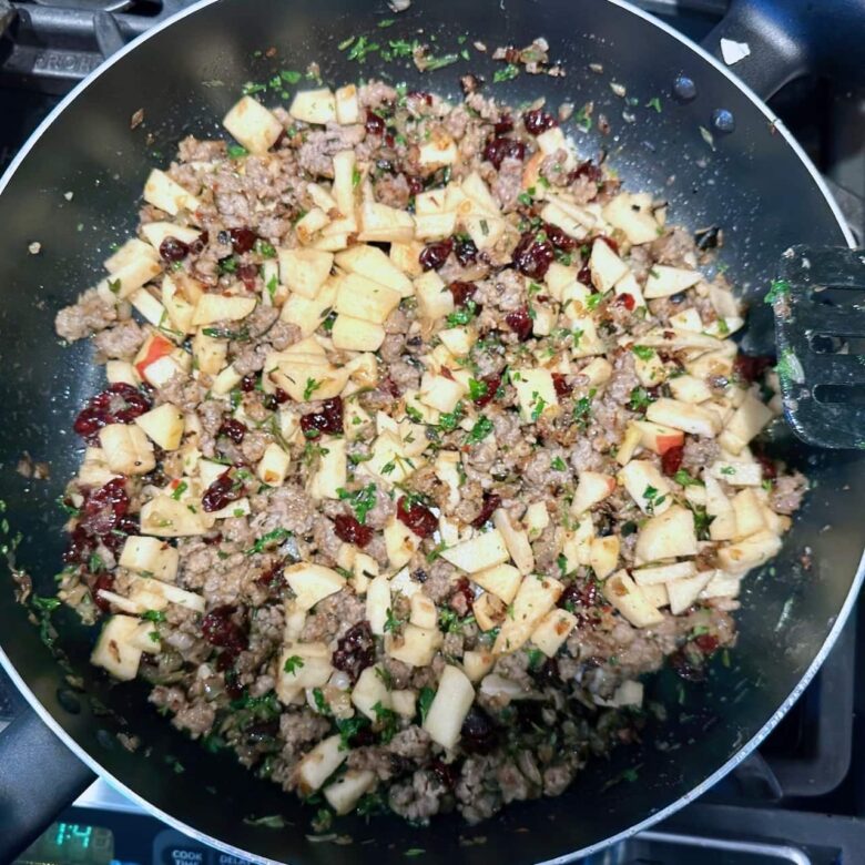 sausage, apples, onions, and herbs cooking in a skillet.
