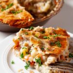 A slice of turkey pot pie on a white plate with a flaky crust.