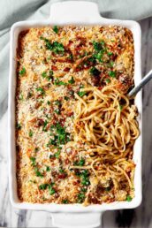 Overhead shot of turkey tetrazzini, topped with breadcrumbs and parsley, with a serving spoon lifting a portion.