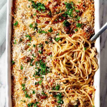 Overhead shot of turkey tetrazzini, topped with breadcrumbs and parsley, with a serving spoon lifting a portion.