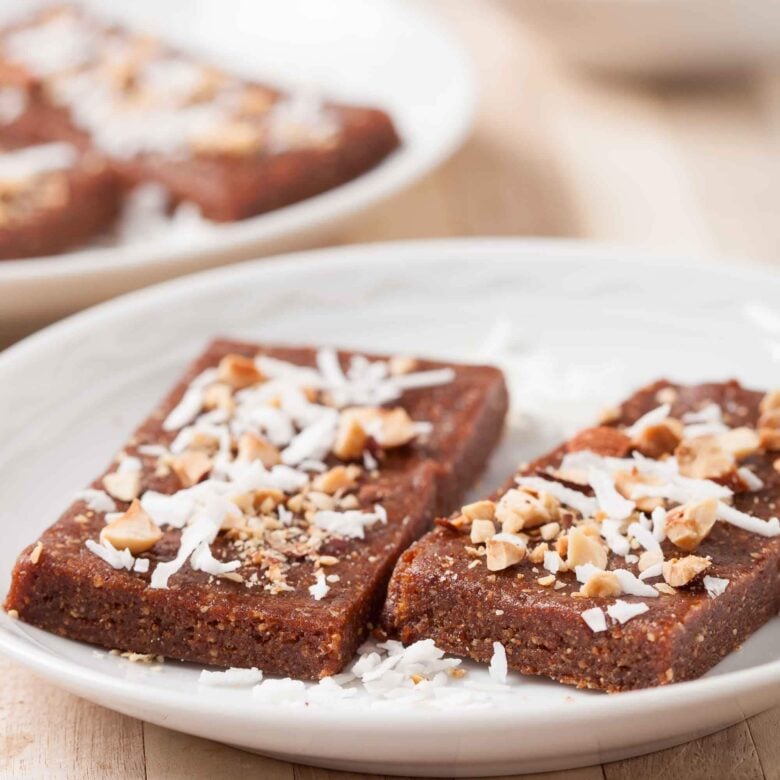Two homemade date bars on a white plate with shredded coconut on top.