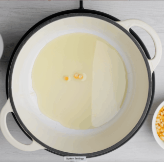Three corn kernels in hot oil in pan for making kettle corn.