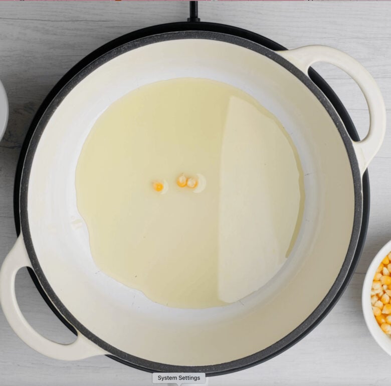 Three corn kernels in hot oil in pan for making kettle corn.