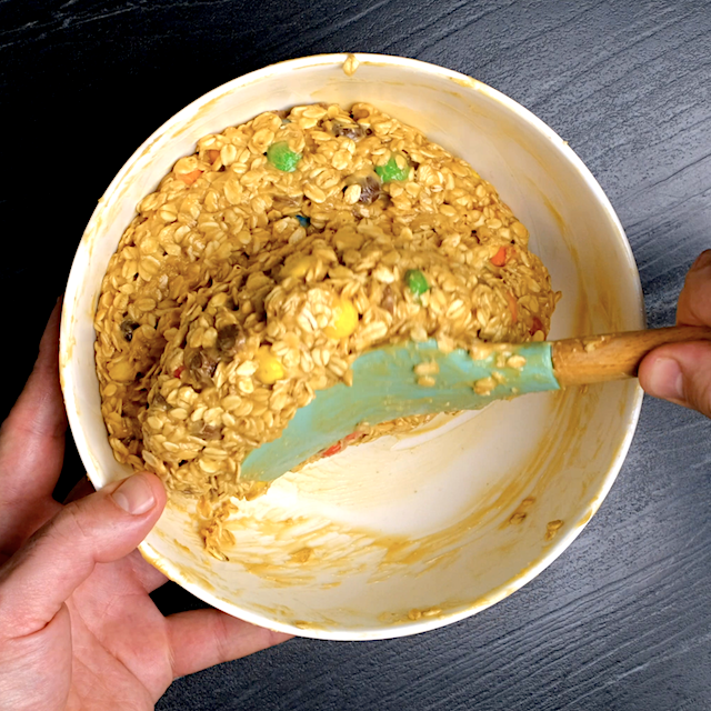 M&Ms, chocolate chips, and oats being mixed into monster cookie dough mixture.