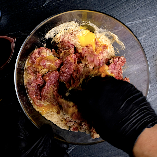 Meatball ingredients being mixed by hand in a glass bowl to make sweet and sour meatballs.