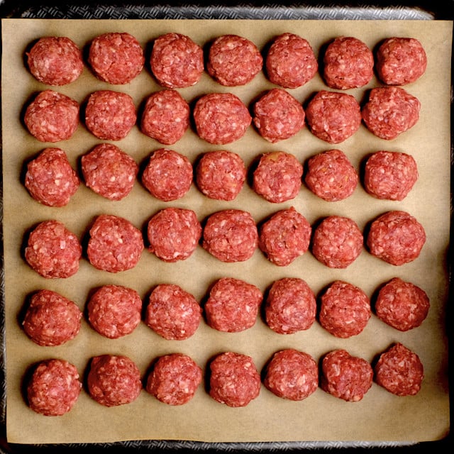 Meatballs placed on a parchment-lined baking sheet, ready to be baked.