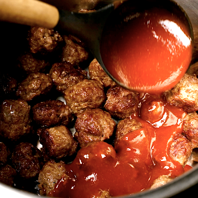 Sweet and sour sauce being poured over baked meatballs in a slow cooker.