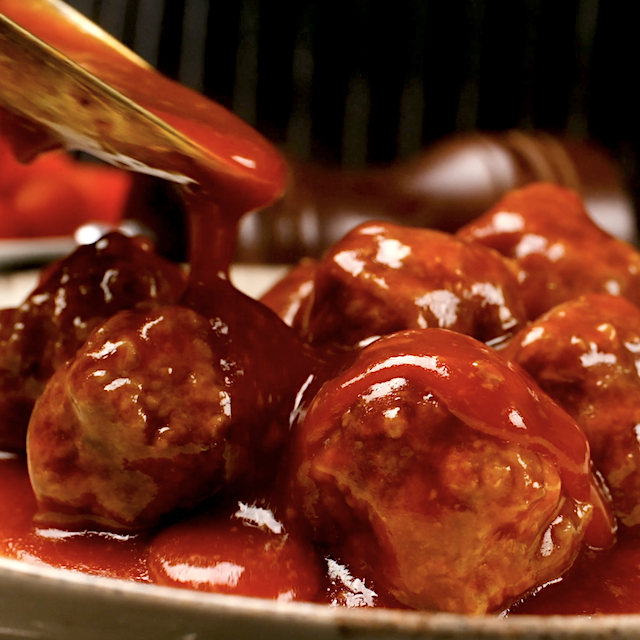 Sauce being poured over sweet and sour meatballs before serving.