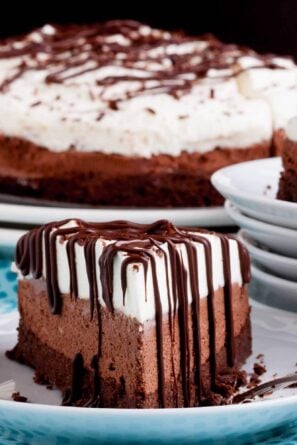 A slice of triple chocolate mouse cake with chocolate drizzle on a plate.