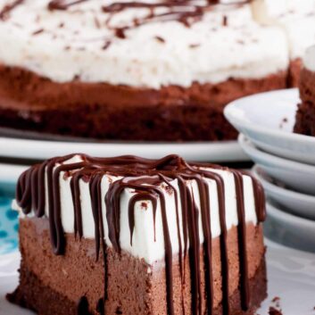 A slice of triple chocolate mouse cake with chocolate drizzle on a plate.