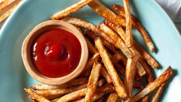 A blue plate with extra crispy, golden-brown air fryer French fries and a bowl of ketchup.