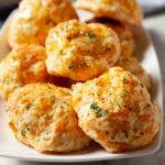 Closeup shot of a plate of freshly baked, golden-brown cheddar bay biscuits garnished with herbs.