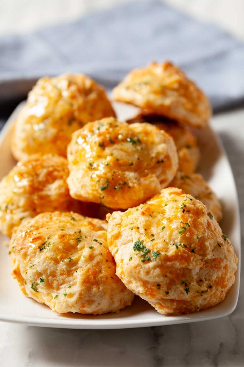 A plate of freshly baked, golden-brown cheddar bay biscuits garnished with herbs.