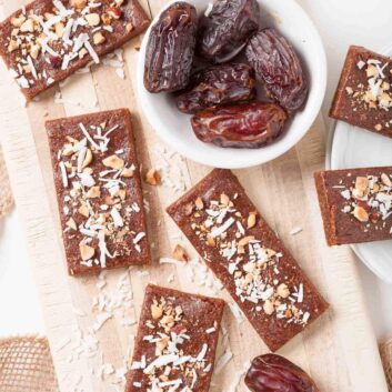 Rectangular date bars topped with shredded coconut and nuts are arranged on a wooden board.
