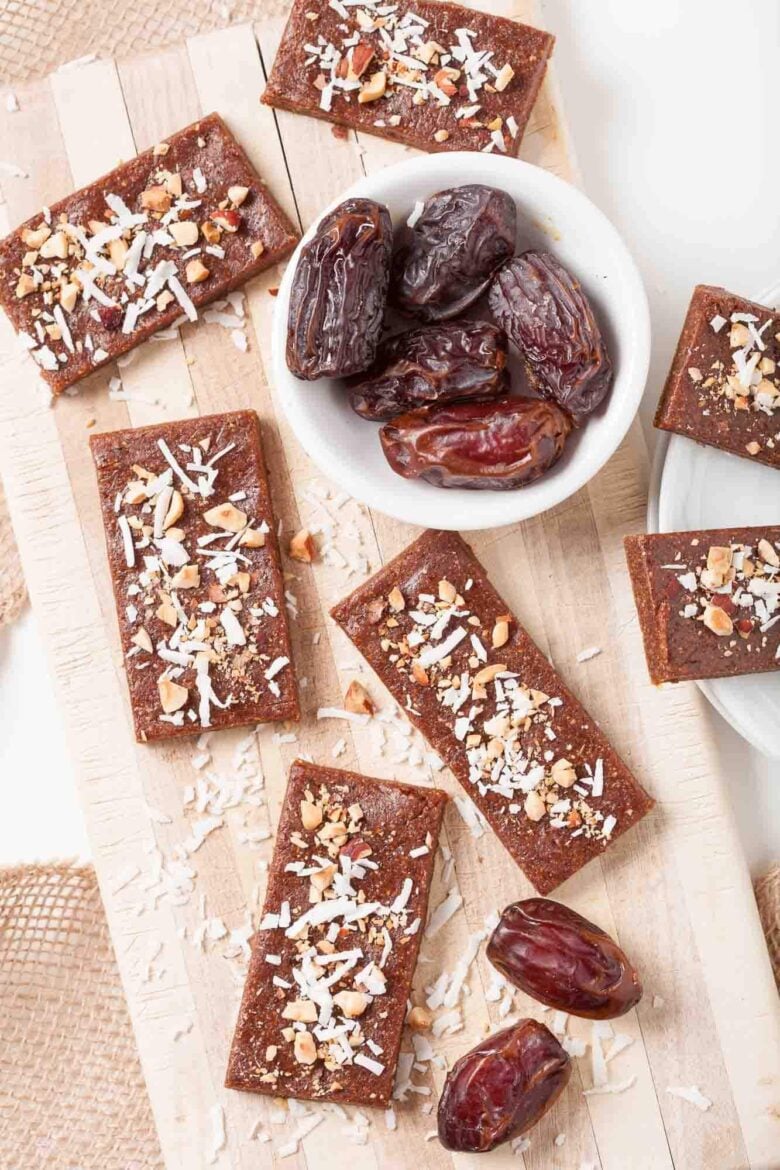 Rectangular date bars topped with shredded coconut and nuts are arranged on a wooden board.