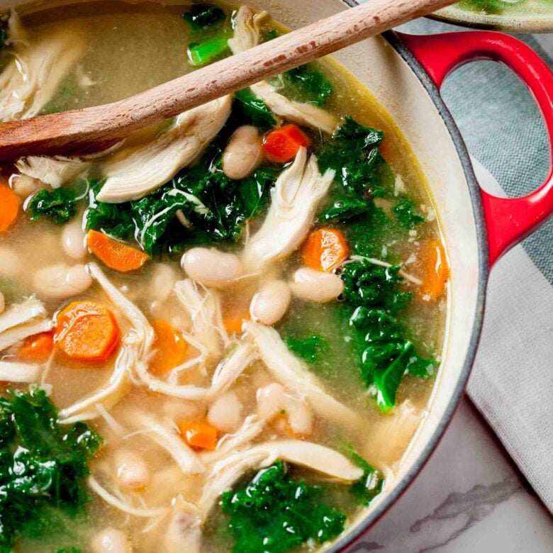 Overhead shot of bowl of Chicken White Bean Soup featuring shredded chicken, white beans, kale, carrots, and rice.