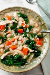 A bowl of Chicken White Bean Soup containing shredded chicken, white beans, kale, carrots, and rice, with a spoon on the side.