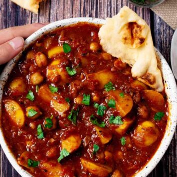 Overhead shot of a bowl of chickpea curry with chopped herbs and garnished with naan bread.