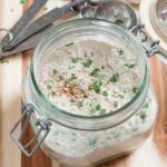 A glass jar containing all-natural homemade ranch seasoning on a wooden surface.