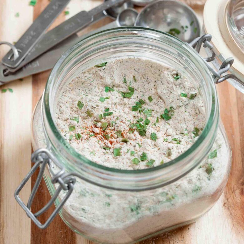 A glass jar containing all-natural homemade ranch seasoning on a wooden surface.