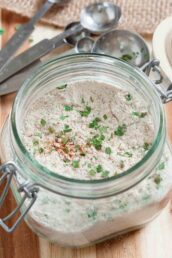 A glass jar containing all-natural homemade ranch seasoning on a wooden surface.