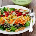 Closeup shot of southwest chopped salad with dressing served in a white plate with a fork on the side.