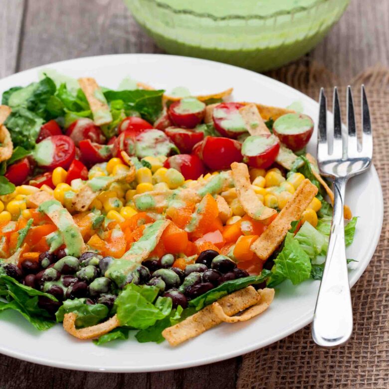 Closeup shot of southwest chopped salad with dressing served in a white plate with a fork on the side.