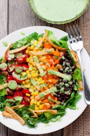 Overhead shot of a colorful Southwest chopped salad with romaine lettuce, cherry tomatoes, corn, black beans, diced bell peppers, tortilla strips, and green dressing.