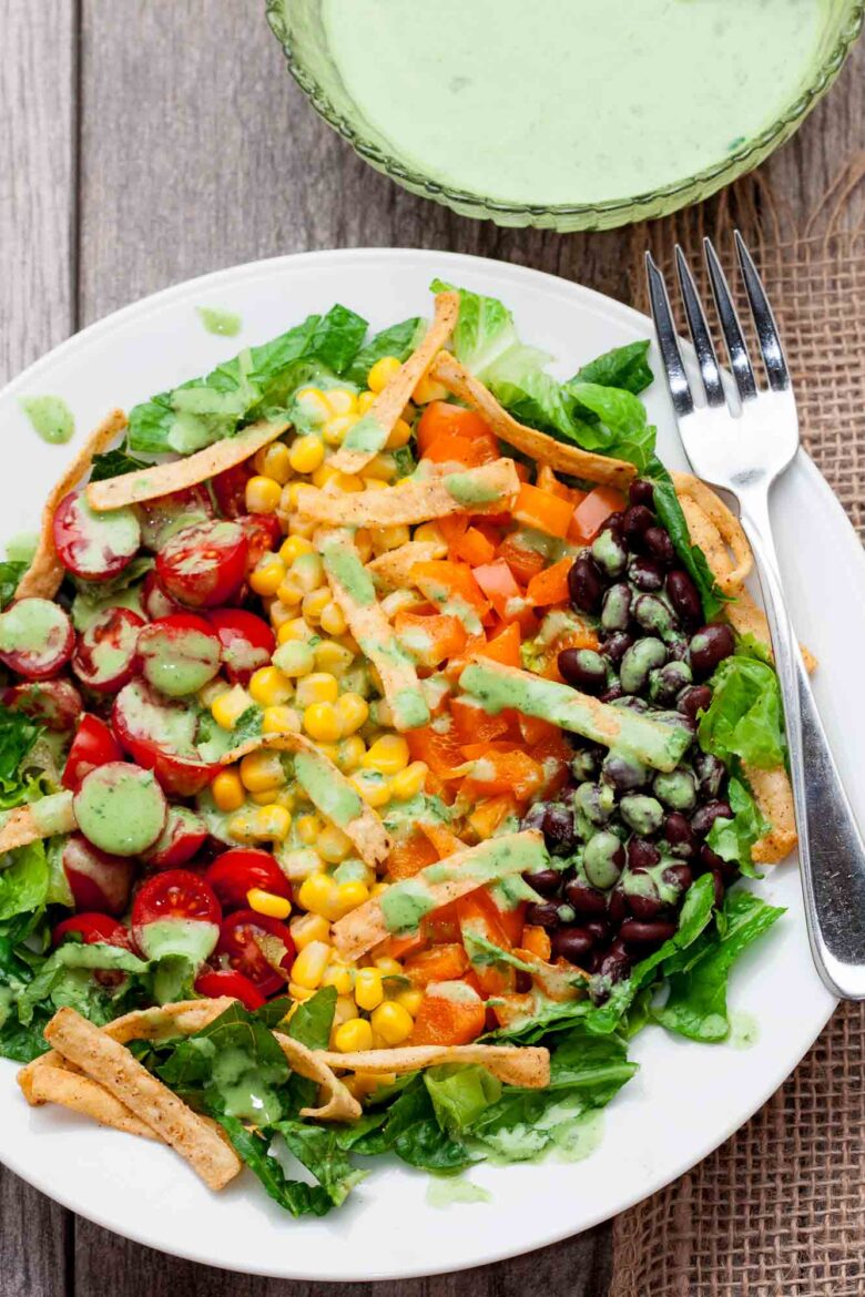 Overhead shot of a colorful Southwest chopped salad with romaine lettuce, cherry tomatoes, corn, black beans, diced bell peppers, tortilla strips, and green dressing.