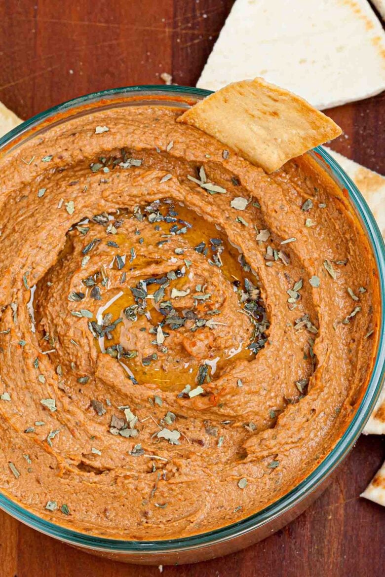 A closeup shot of a bowl of sun dried tomato hummus garnished with herbs.