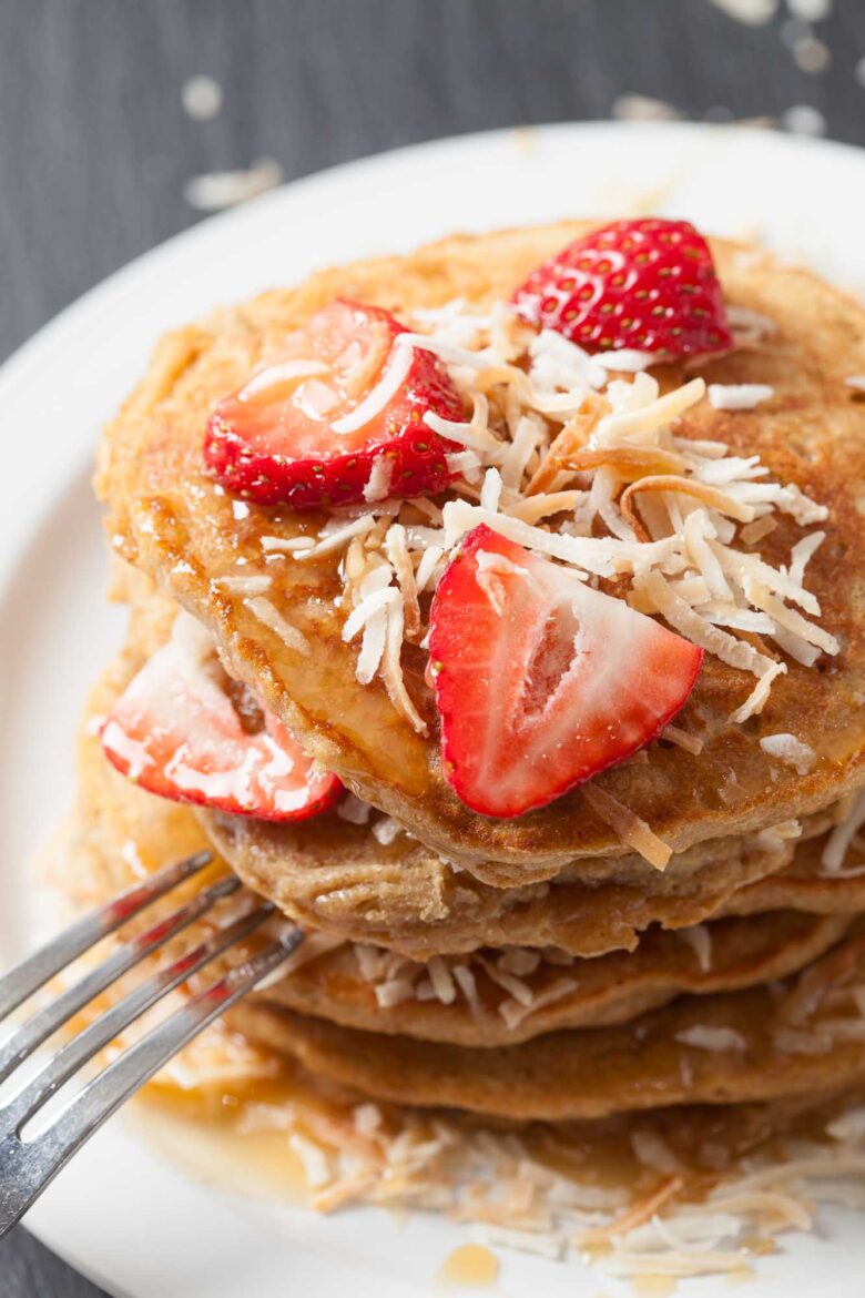 Overhead shot of fluffy coconut pancakes topped with sliced strawberries and shredded coconut