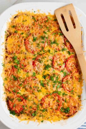 Hash brown tomato breakfast casserole with sliced tomatoes, shredded cheese, and herbs in a white casserole dish.