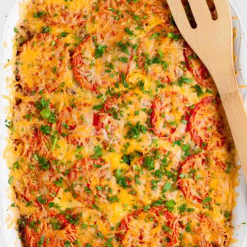 Hash brown tomato breakfast casserole with sliced tomatoes, shredded cheese, and herbs in a white casserole dish.