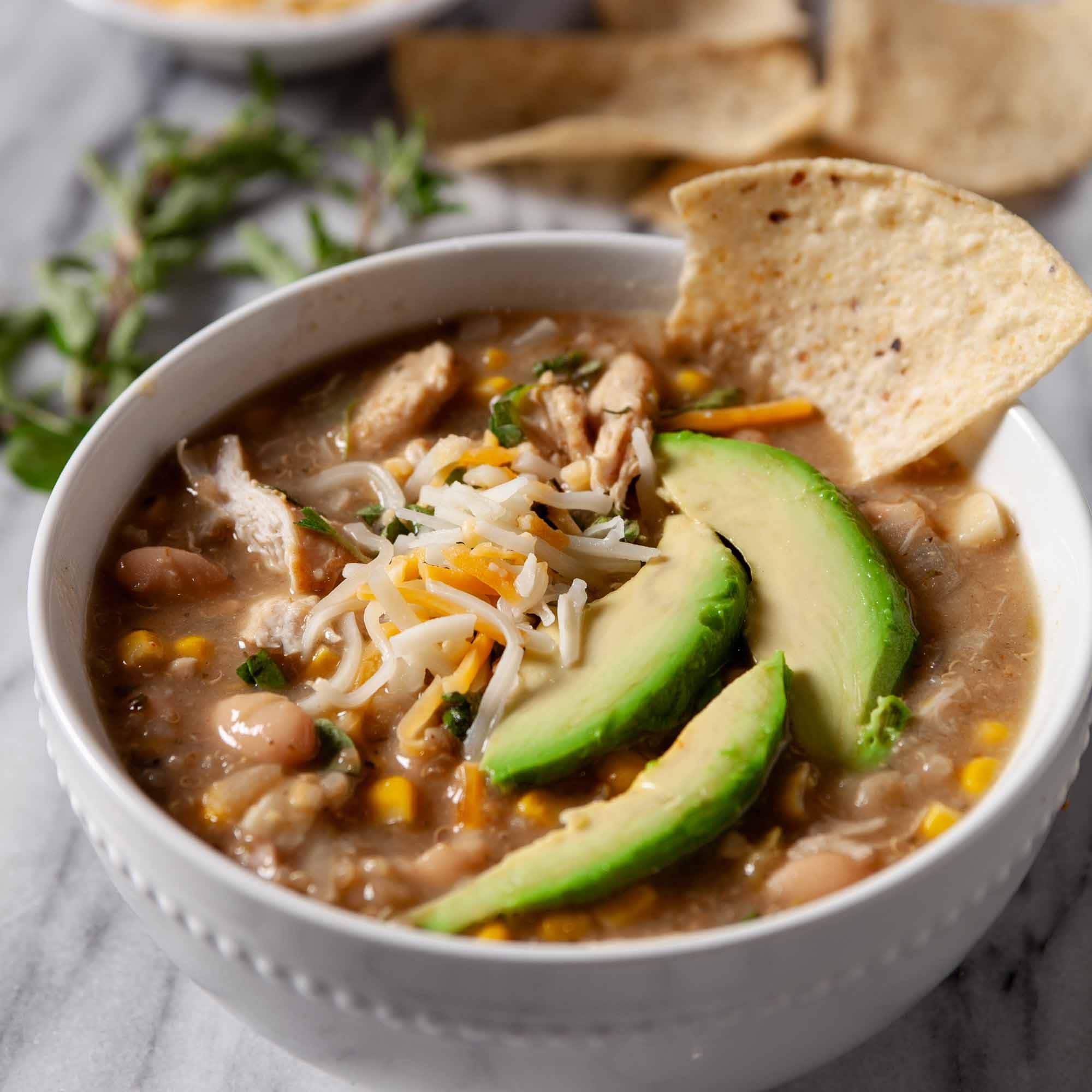 Close-up shot of a bowl of healthy white chicken chili, garnished with sliced avocados.