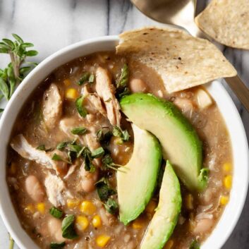 An overhead shot of a bowl of healthy white chicken chili, garnished with sliced avocados.