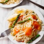 Overhead shot of a place of lemon pasta pasta with smoked salmon, asparagus and lemon wedges.