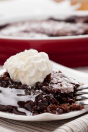 Closeup shot of a slice of molted chocolate cake with a gooey, molten center and stabilized whipped cream on top.