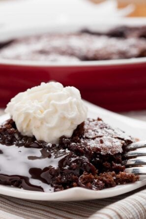 Closeup shot of a slice of molted chocolate cake with a gooey, molten center and stabilized whipped cream on top.