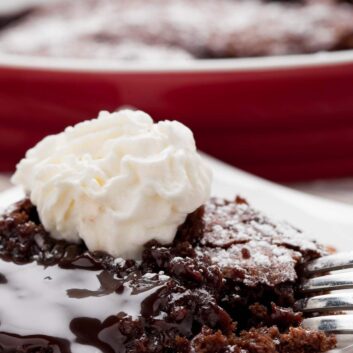 Closeup shot of a slice of molted chocolate cake with a gooey, molten center and stabilized whipped cream on top.