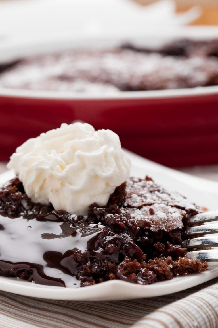 Closeup shot of a slice of molted chocolate cake with a gooey, molten center and stabilized whipped cream on top.
