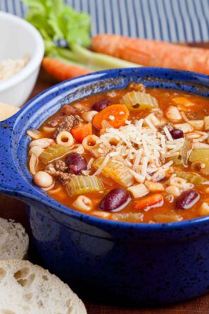 A closeup shot of a bowl of pasta e fagioli with grated parmesan cheese on top.