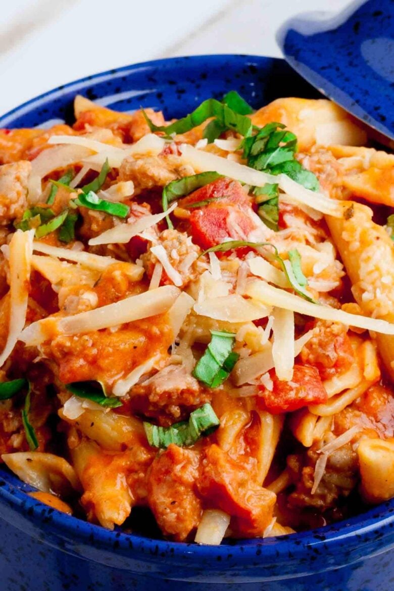 Closeup shot of a bowl of penne with vodka sauce, garnished with fresh basil leaves and parmesan cheese.