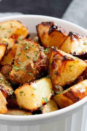 A white dish filled with golden-brown ranch roasted potatoes, garnished with chopped herbs.