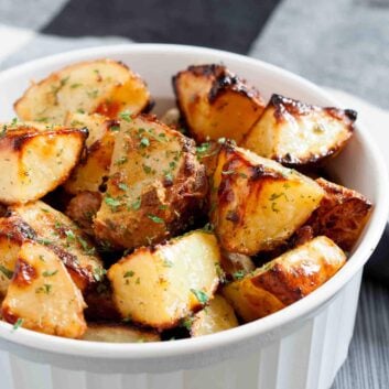 A white dish filled with golden-brown ranch roasted potatoes, garnished with chopped herbs.