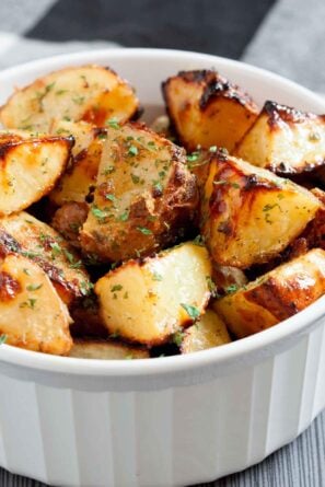 Closeup shot of a dish filled with golden-brown ranch roasted potatoes, garnished with chopped herbs.