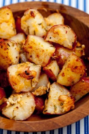 A closeup shot of a wooden bowl filled with roasted red potato seasoned with herbs and spices.