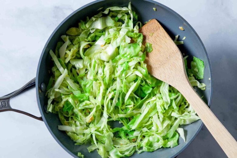 Cabbage being sautéed in a pan to make sautéed cabbage.